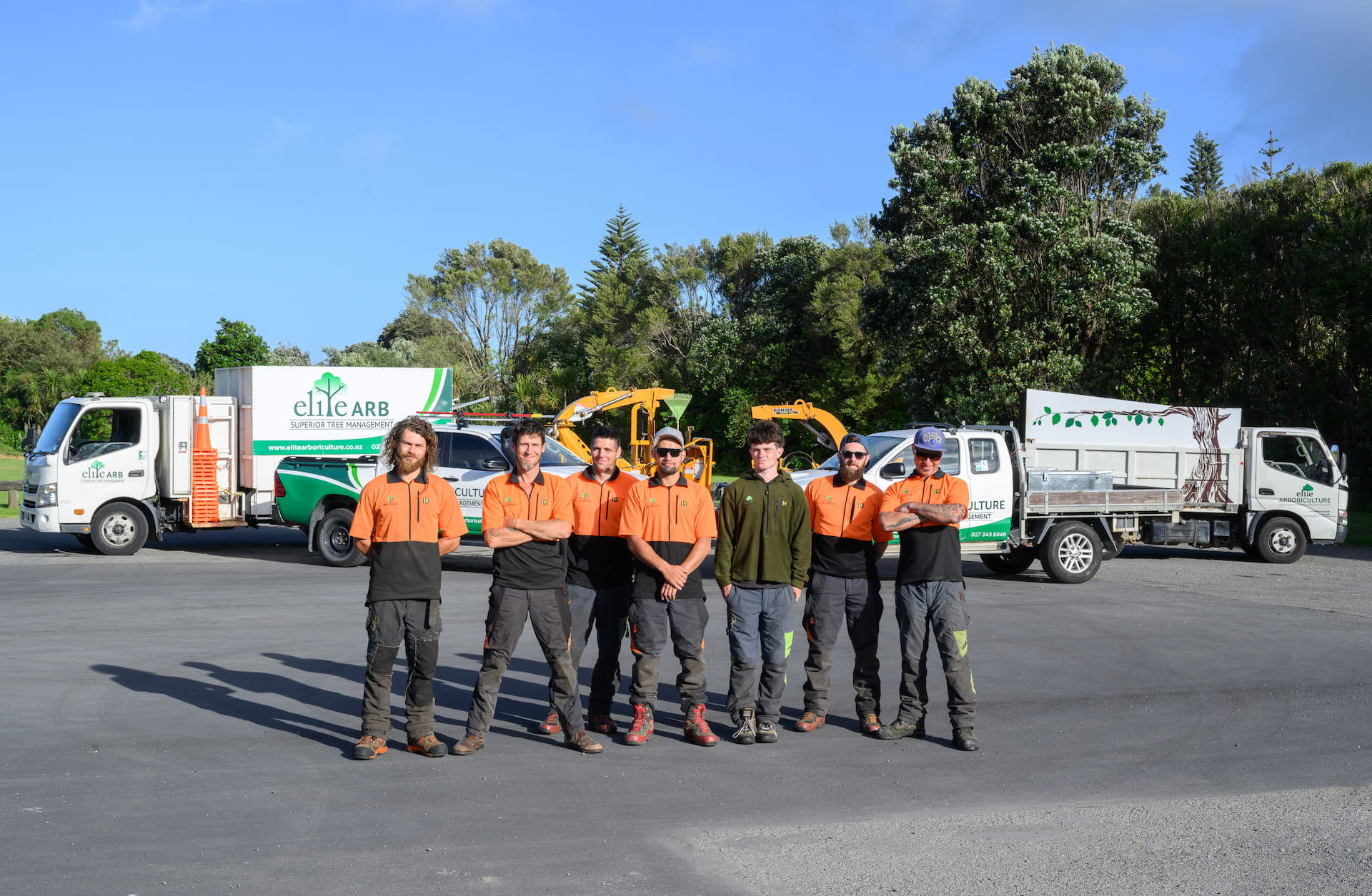 A landscape image of Elite Arboriculture professionals standing in front of their trucks and tools.